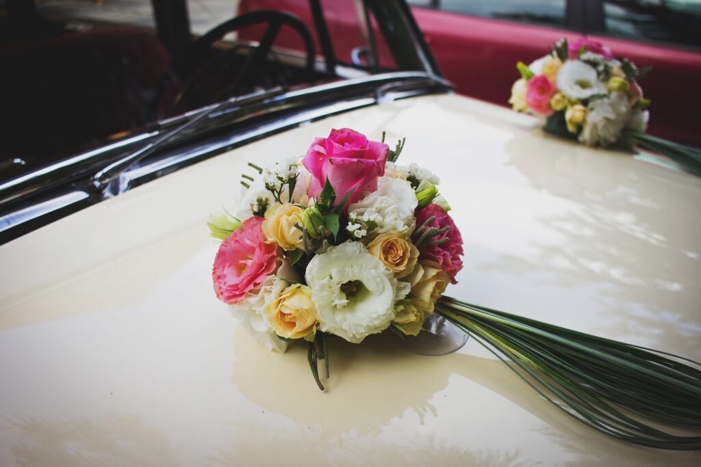 Bloemstuk met roze, witte en gele bloemen op de motorkap van een crèmekleurige trouwauto