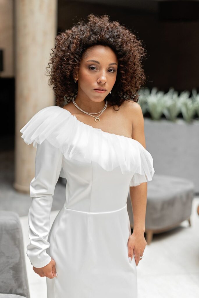Bruid met volle natuurlijke krullen in een witte one-shoulder jurk