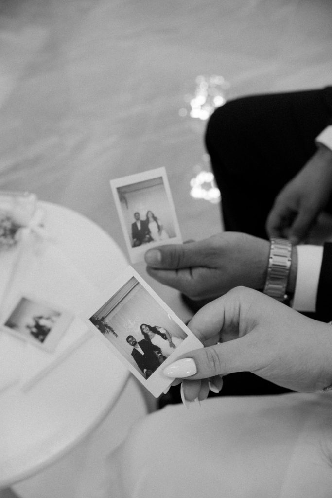 Zwart-witte close-up van een bruidspaar dat instantfoto’s van hun bruiloft vasthoudt