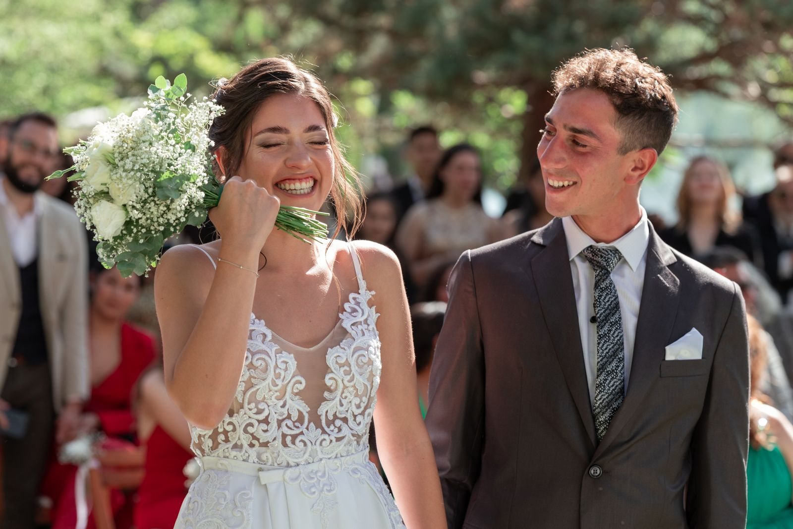 Lachend bruidspaar loopt na de ceremonie buiten tussen de gasten door, de bruid met een boeket witte bloemen