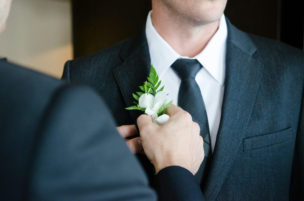 Bruidegom in een donkerblauw pak met stropdas krijgt een witte corsage op zijn revers gespeld