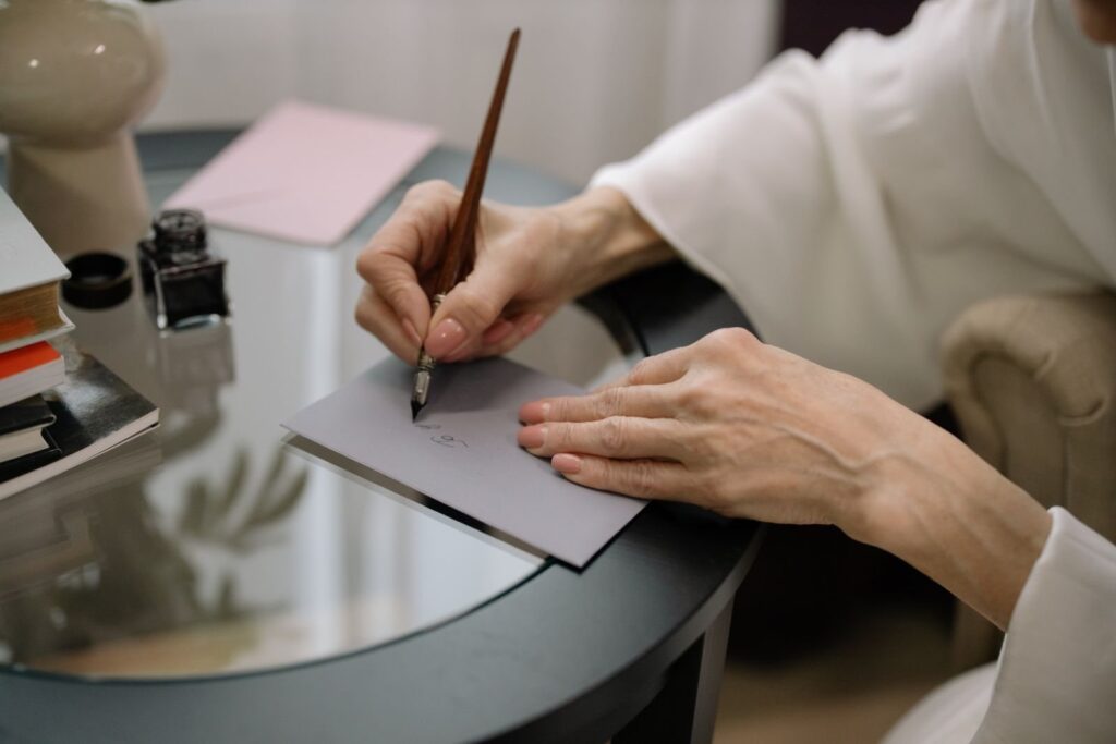 Handen die met een vulpen een adres op een grijze envelop schrijven