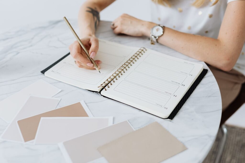 Vrouw schrijft in een agenda op een marmeren tafel, omringd door papieren kleurstalen