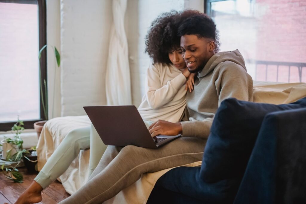 Stel zit lachend samen op de bank en kijkt naar een laptop