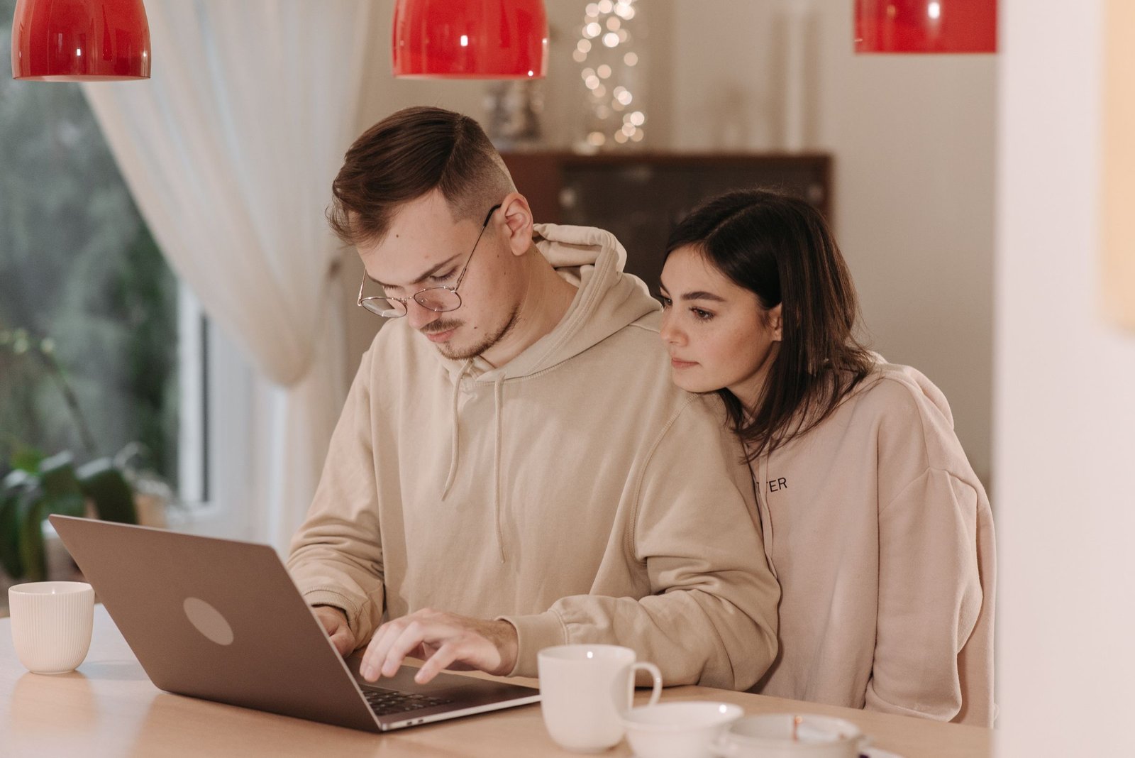 Jong stel zit samen met laptop en koffie aan tafel en plant hun bruiloft budget