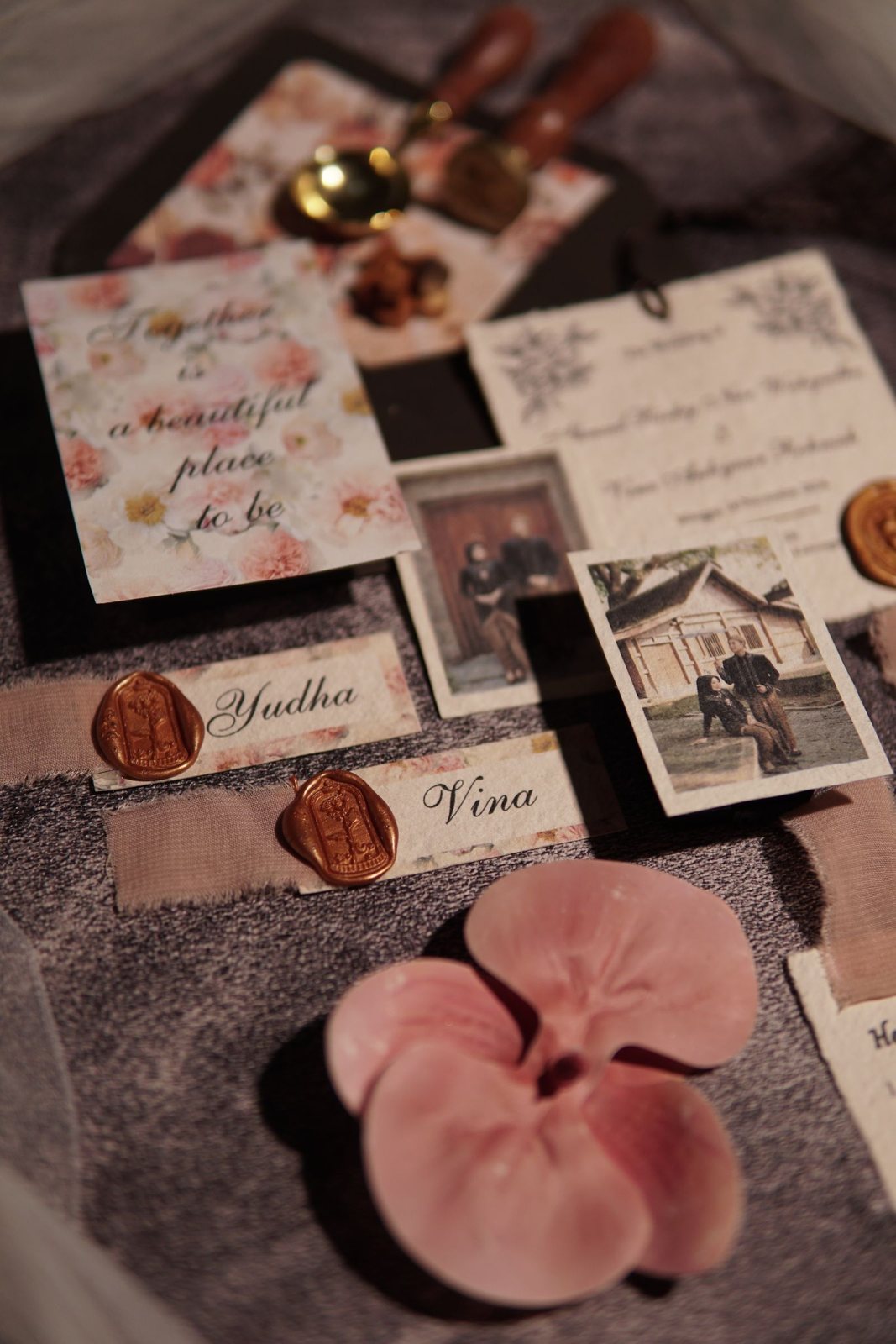 Flatlay van trouwkaarten met bloemenprint, naamkaartjes met lakzegels en orchideeblaadjes