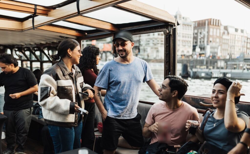 Vriendengroep met drankjes lacht en praat aan boord van een boot op het water in Amsterdam