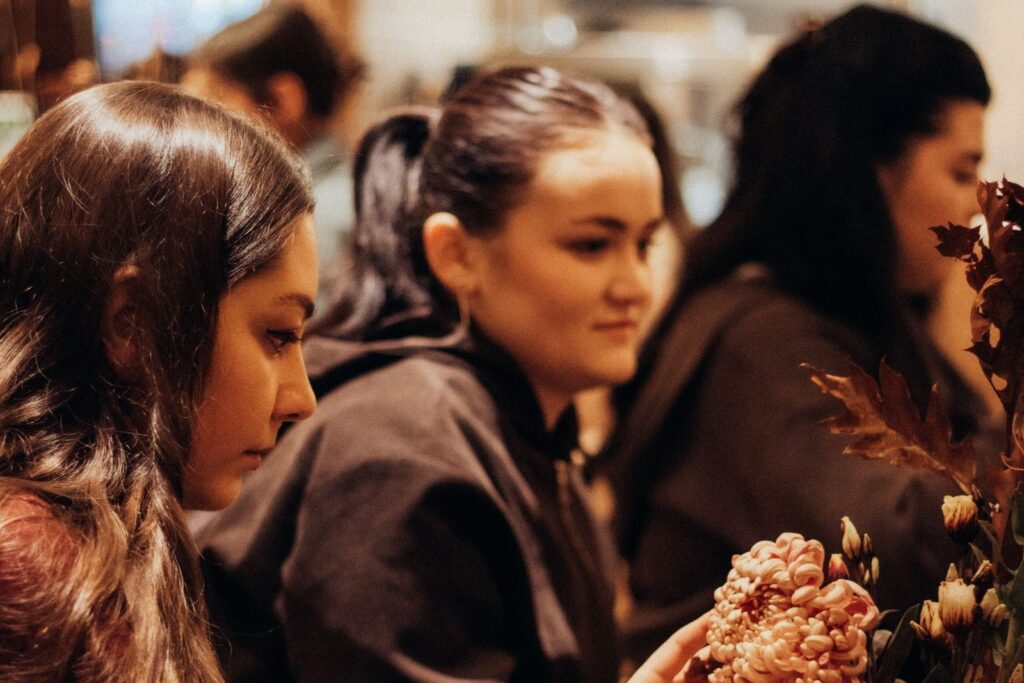 Jonge vrouwen werken geconcentreerd aan bloemstukken tijdens een bloemschikworkshop
