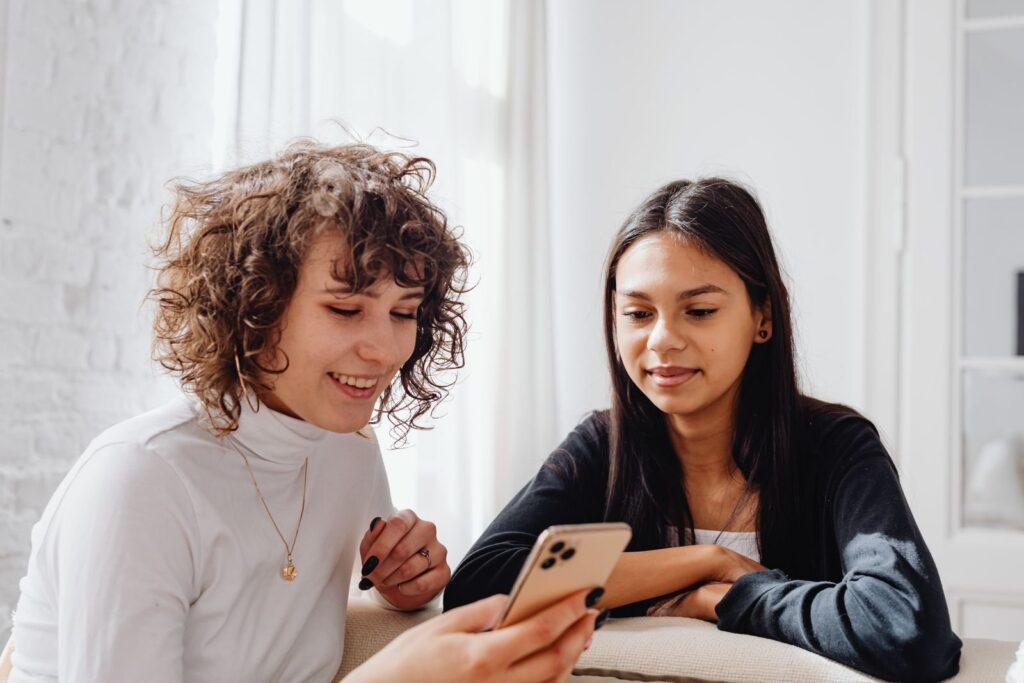 Twee lachende jonge vrouwen kijken samen op een smartphone