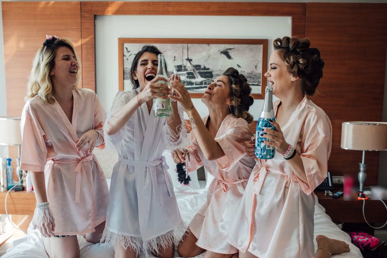 Vier vriendinnen in roze satijnen badjassen proosten lachend met bubbels in een hotelkamer