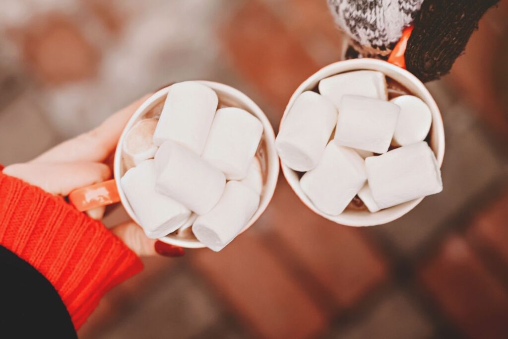 Twee handen met mokken warme chocolademelk vol marshmallows